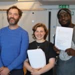 Three performers pose for the camera holding show scripts